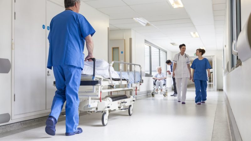 20705732 - male nurse pushing stretcher gurney bed in hospital corridor with doctors & senior female patient